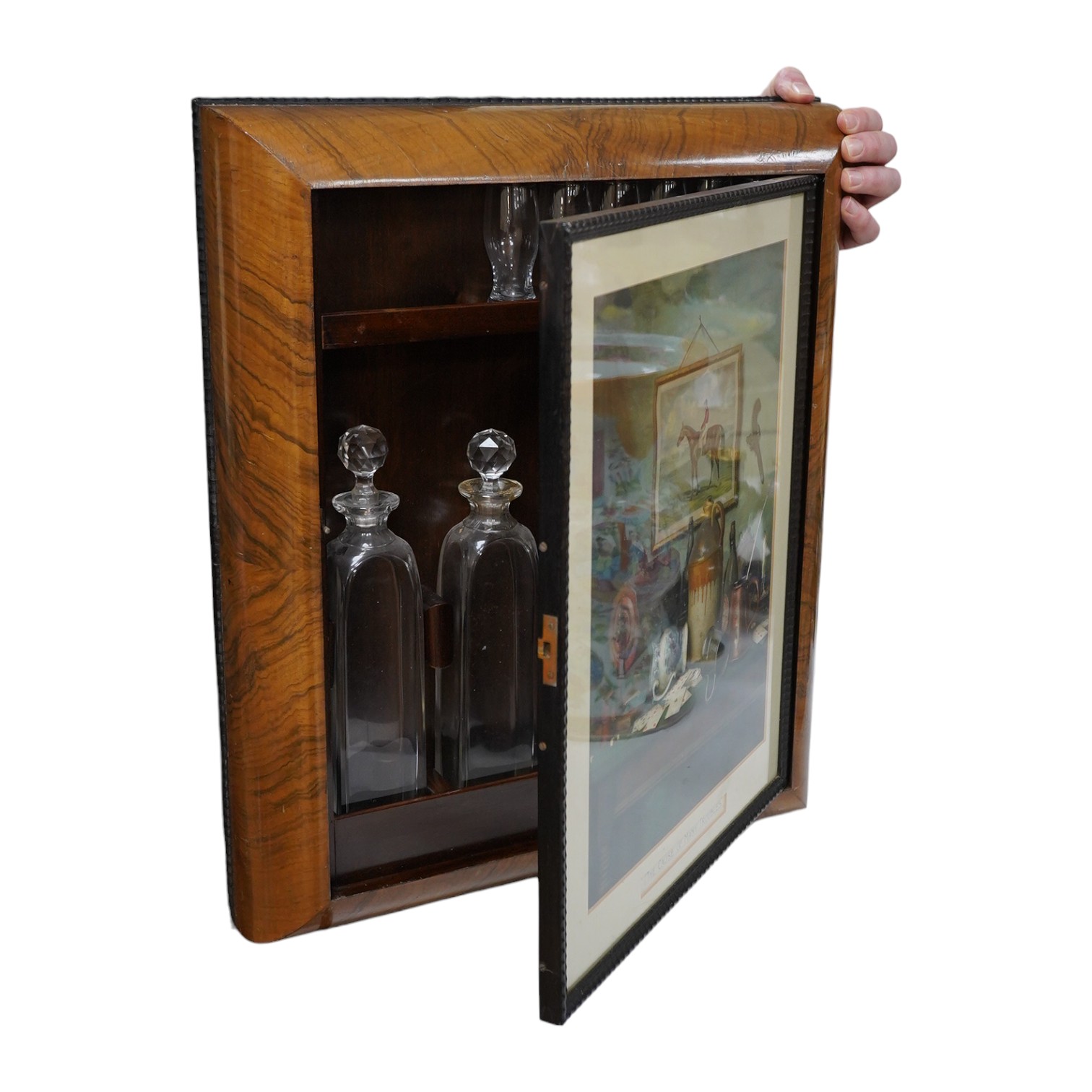 Asprey of London, a cushion-moulded walnut decanter wall cabinet, chromolithograph enclosing four cut glass decanters and six shot glasses, 57cm high, 37.5cm wide. Condition - good.